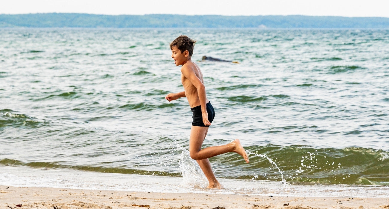 Dreng løber på strand i badetøj